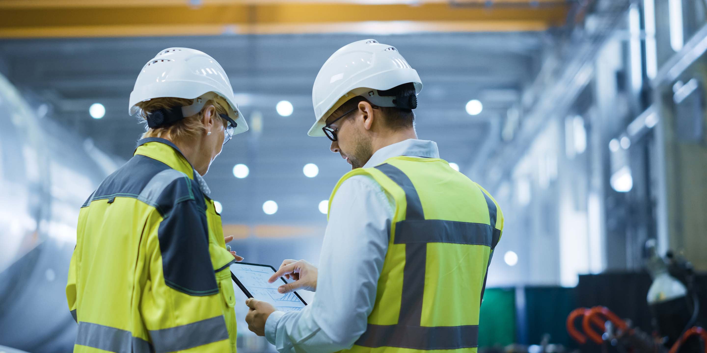 Two Heavy Industry Engineers Stand in Pipe Manufacturing Factory, Use Digital Tablet Computer, Have Discussion. Large Pipe Assembled. Design and Construction of Oil, Gas and Fuels Transport Pipeline