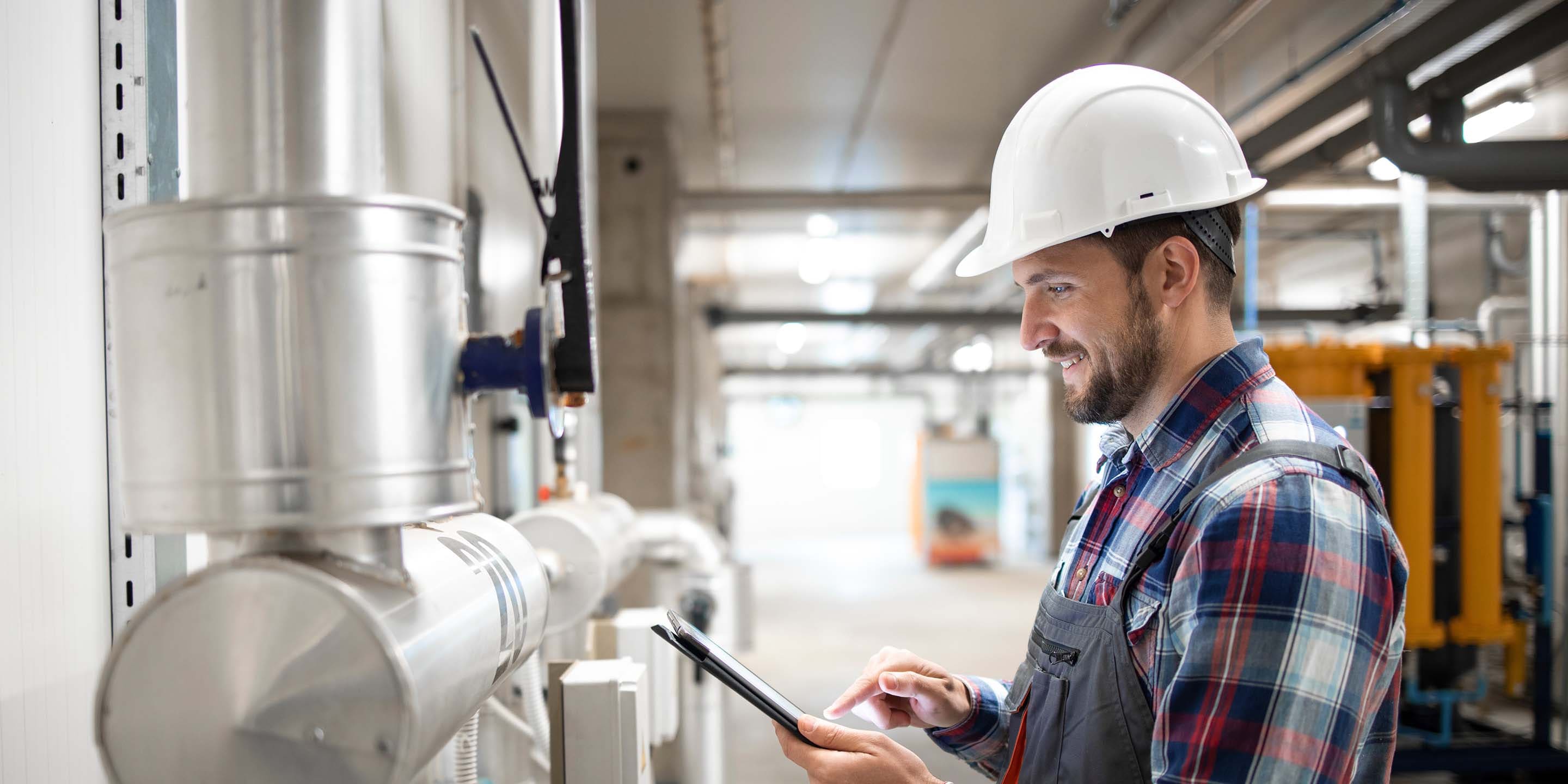 Industrial engineer worker holding tablet computer and setting parameters of heating system in factory boiler room.