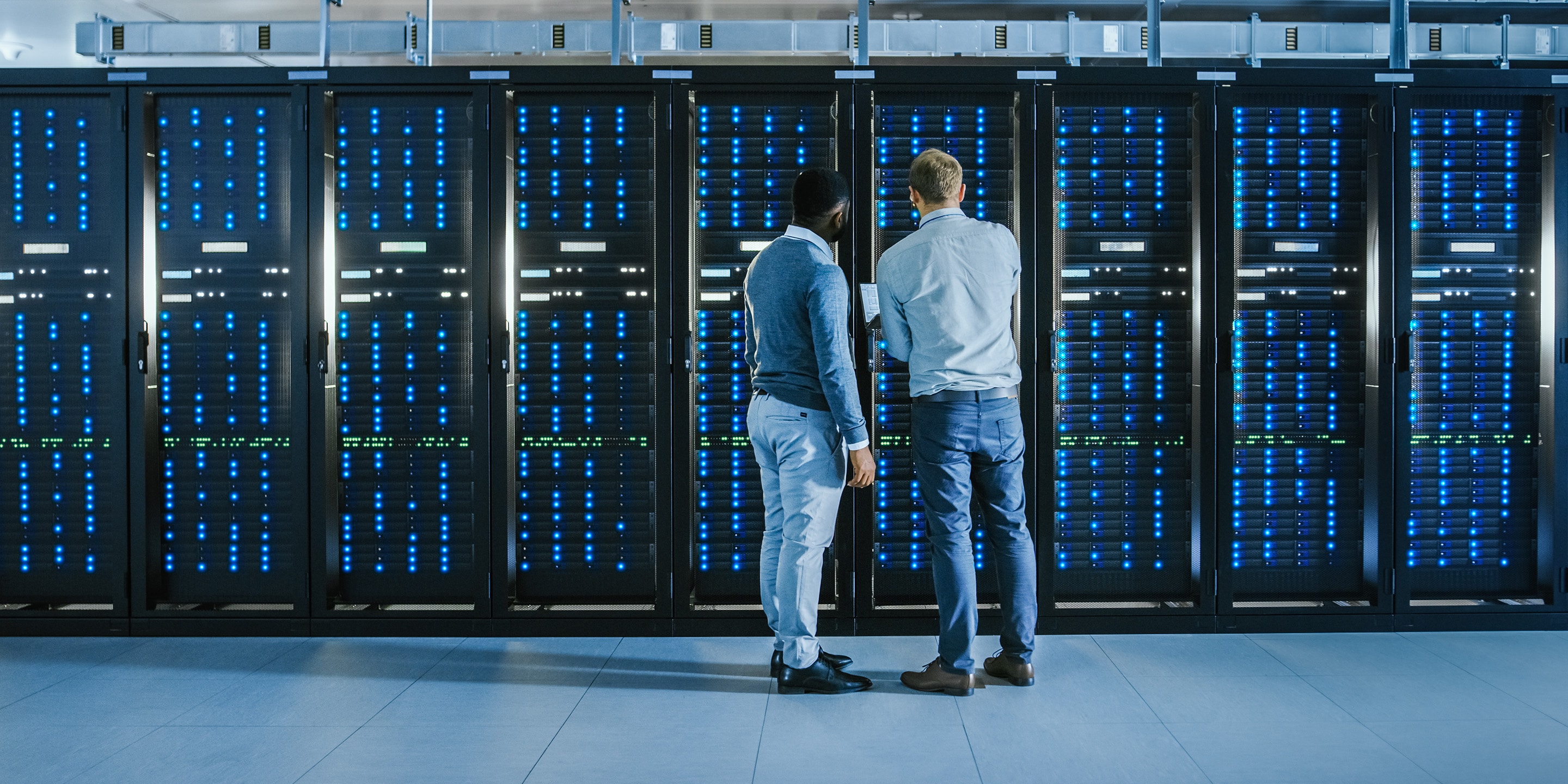 Two individuals stand in front of illuminated server racks in a data center, highlighting infrastructure monitoring and IT operations.