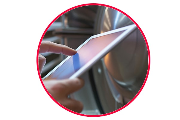 Closeup of a worker's hand using a tablet with a gas turbine in the background